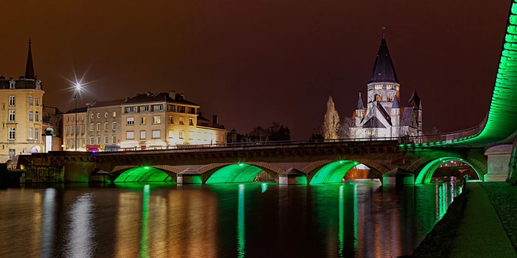 Metz le Temple Neuf de nuit vue des quais avec l'eau et le pont allumé illuminé en vert